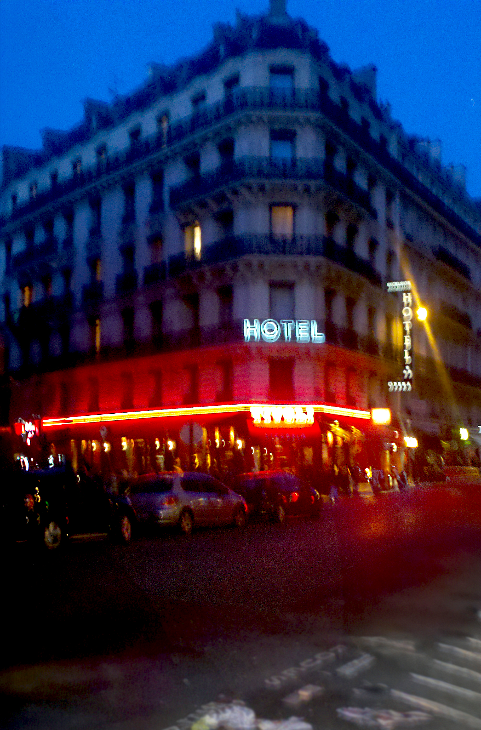  Nighttime corner hotel with neon signs and blurred car lights on a city street.